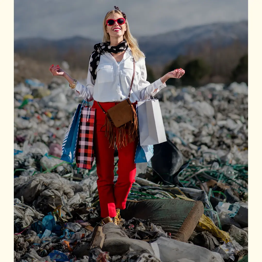 Woman holding shopping bags while standing in a landfill full of discarded clothing, symbolising the environmental impact of fast-fashion waste.
