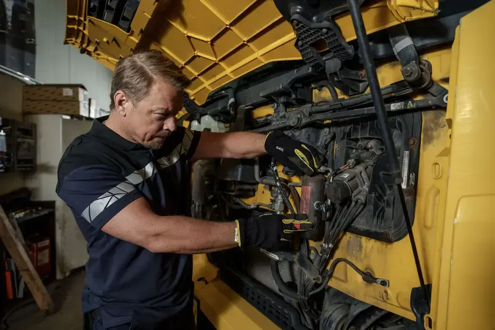 Mechanic wearing recycled and organic workwear polo while repairing engine components